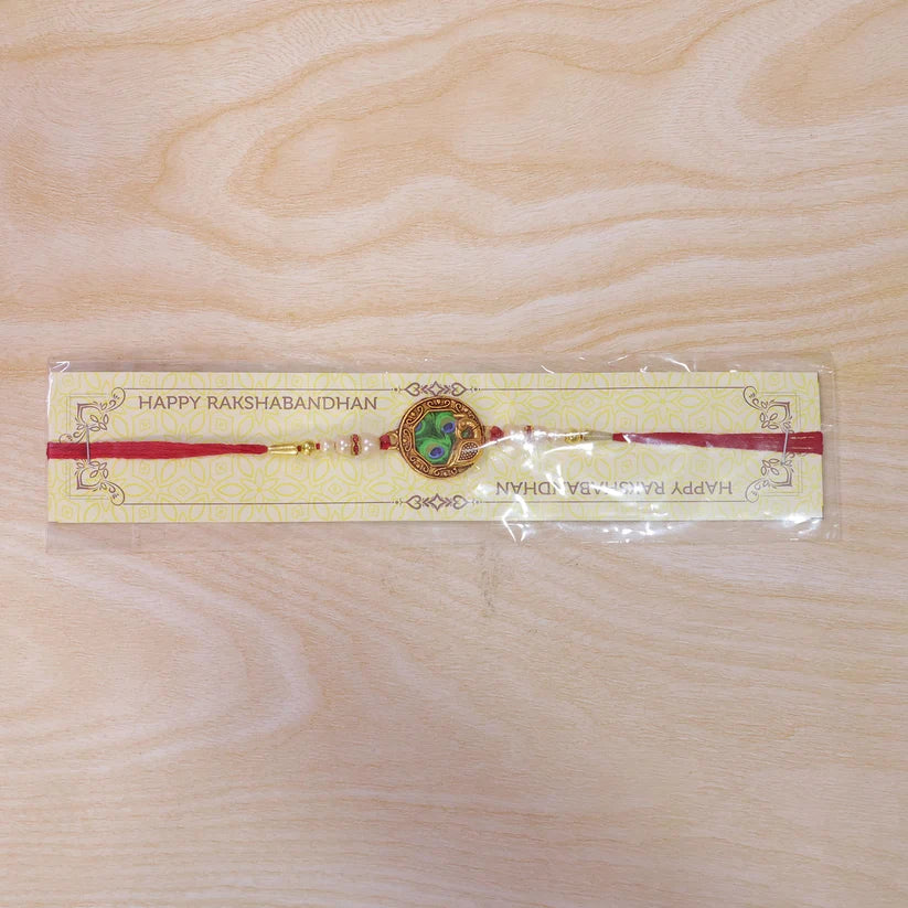 Elegant Rakhi With Peacock Feather Design And Pearl Bead Accents On Red Thread