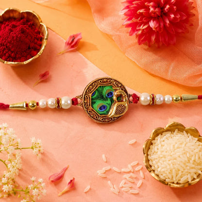 Elegant Rakhi With Peacock Feather Design And Pearl Bead Accents On Red Thread